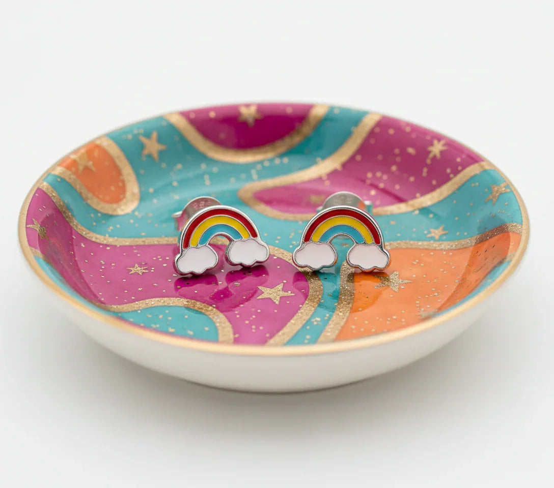 A pair of colorful earrings with rainbow-colored raindrops and clouds are displayed on a decorative plate with a starry background.