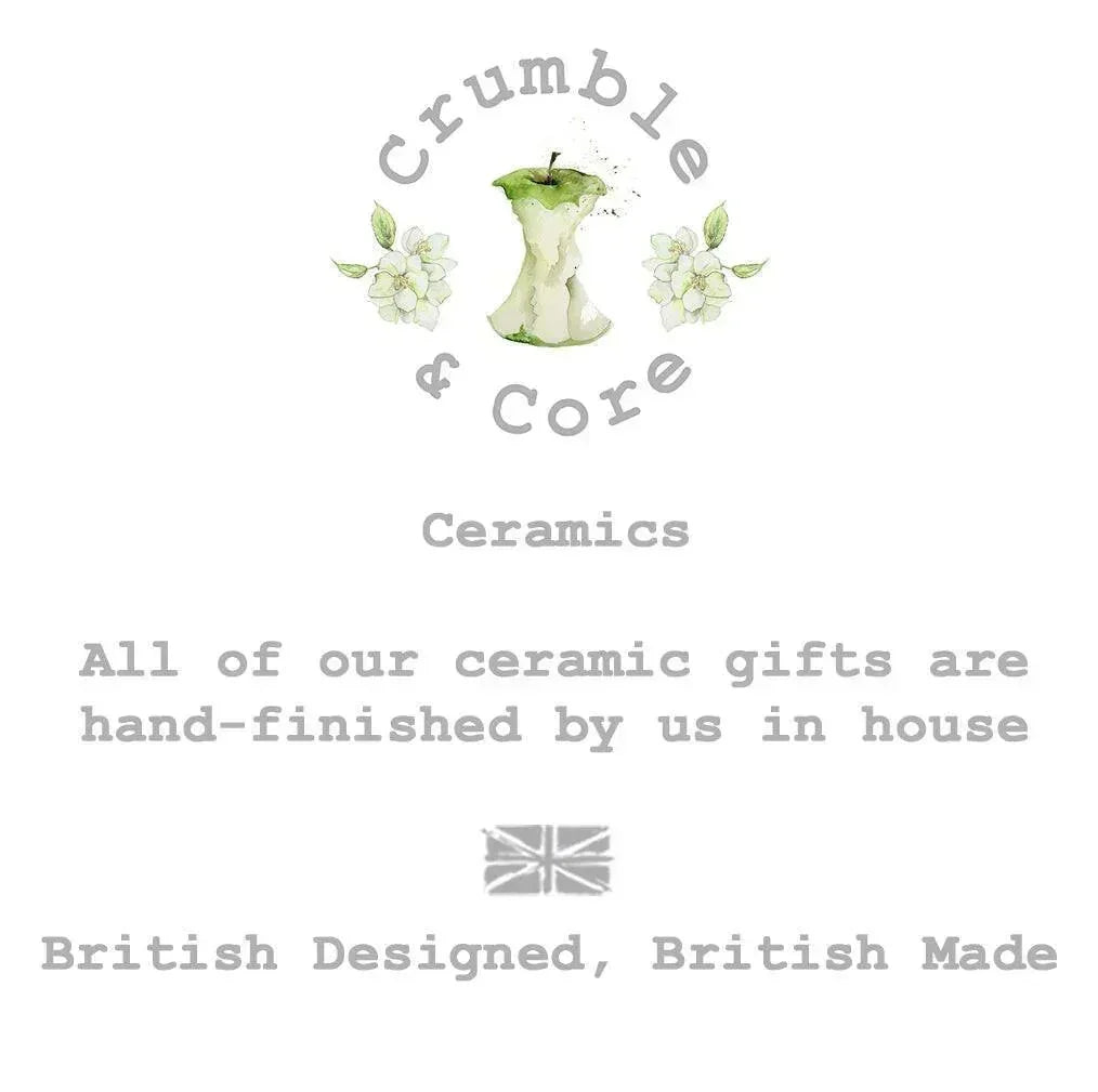 The image is a logo for a company called Crumble & Core, which specializes in ceramics. The logo features an apple with a green stem and leaves, surrounded by white flowers. The company's slogan, "All of our ceramic gifts are hand-finished by us in house", is displayed below the logo. The company's British-designed, British-made tagline is also included in the image.